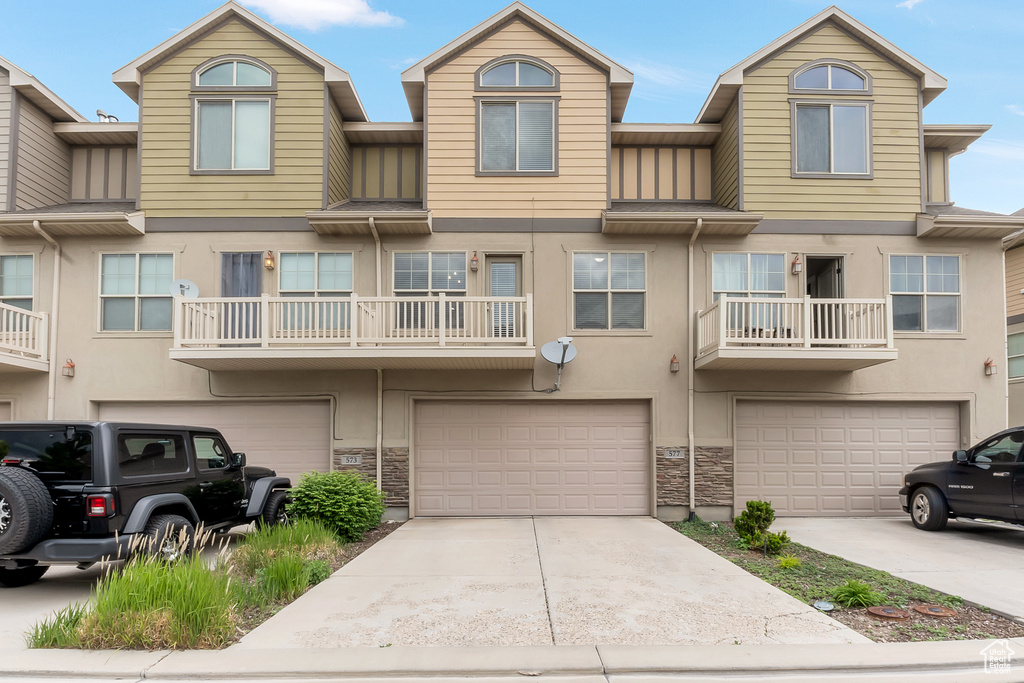 Multi unit property featuring an attached garage, stone siding, stucco siding, and driveway