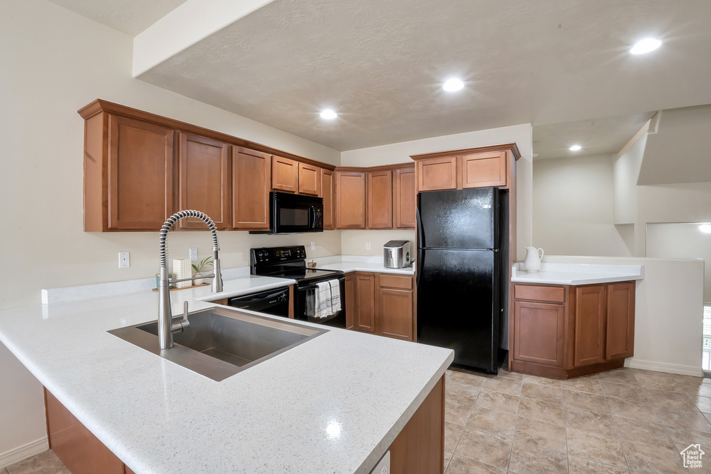 Kitchen with recessed lighting, brown cabinets, a sink, black appliances, and a peninsula