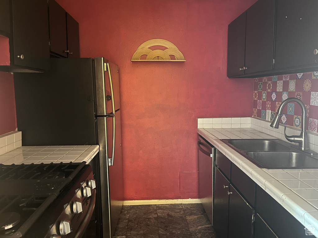 Kitchen with a sink, baseboards, tile counters, and stainless steel appliances