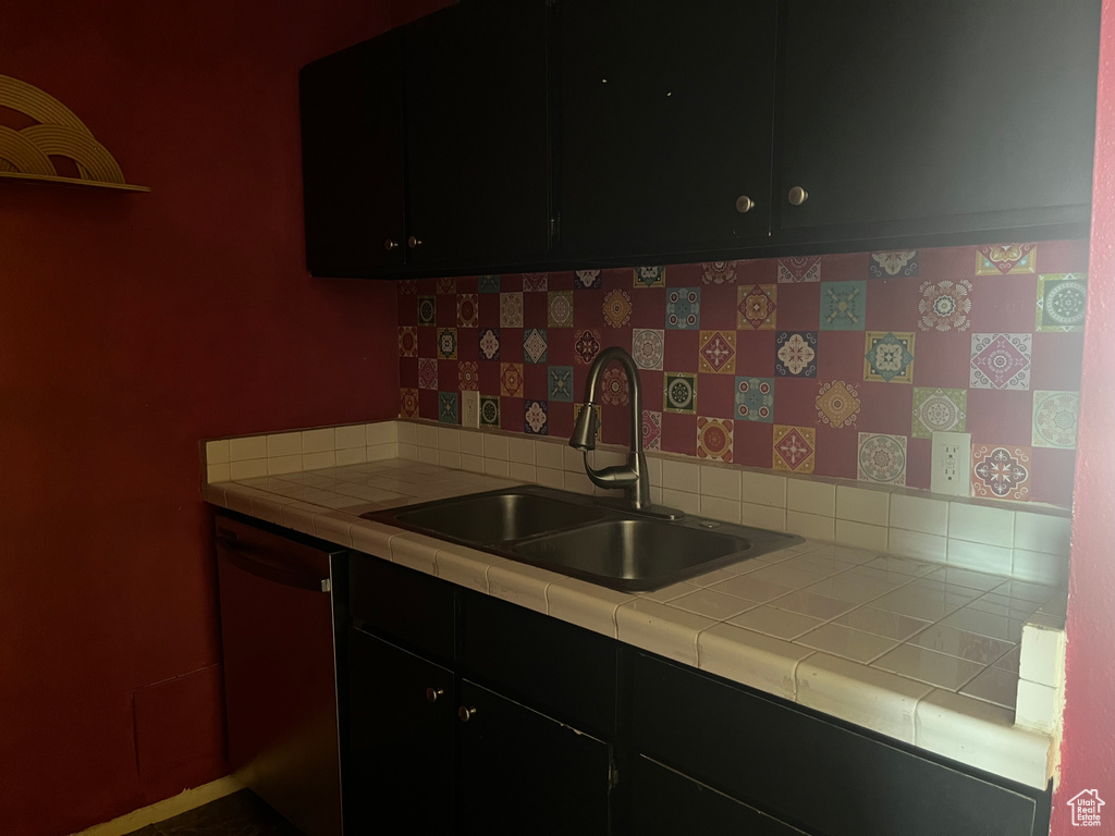 Kitchen featuring tile countertops, tasteful backsplash, dark cabinets, a sink, and dishwasher
