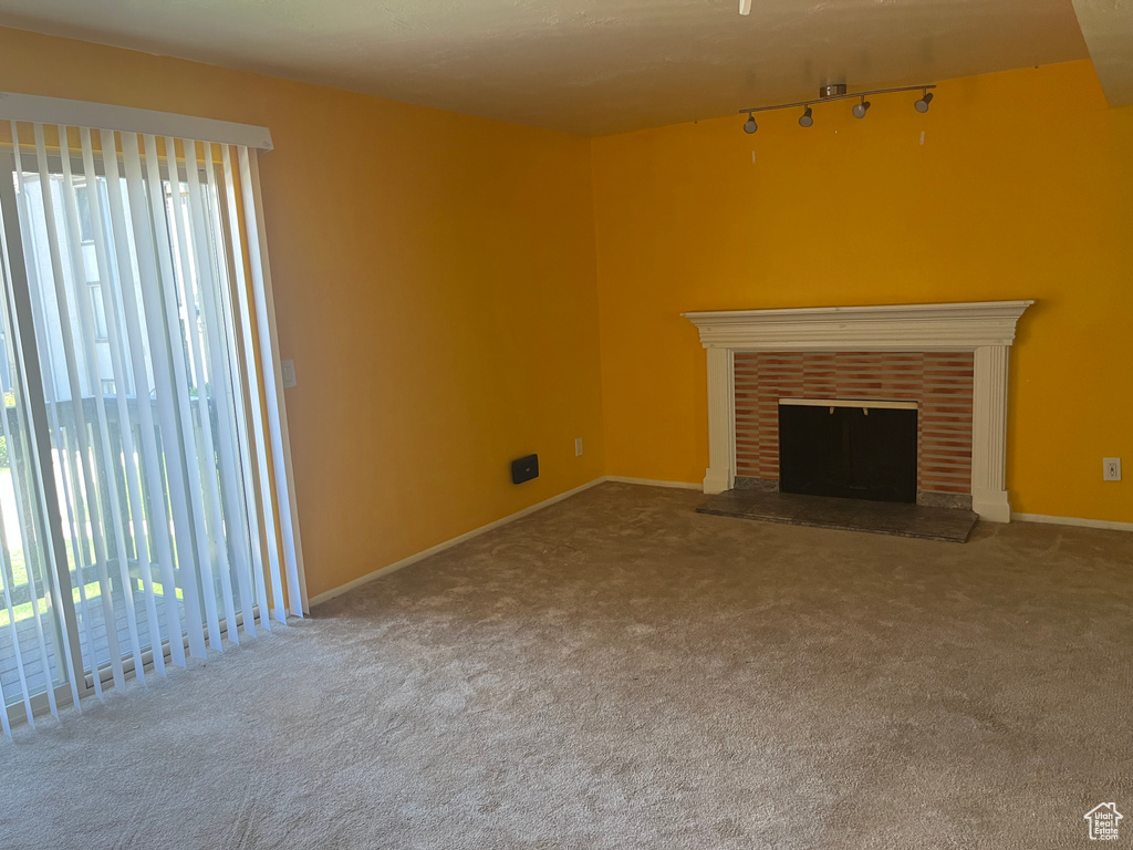 Unfurnished living room featuring rail lighting, plenty of natural light, carpet, and a fireplace