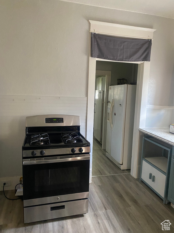 Kitchen featuring white fridge with ice dispenser, light wood-style floors, stainless steel range with gas stovetop, and light countertops