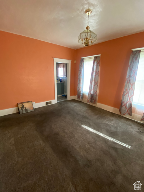 Empty room with a wealth of natural light, dark colored carpet, visible vents, and baseboards