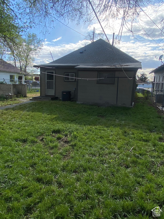 Back of property with a lawn, central AC, fence, and a shingled roof
