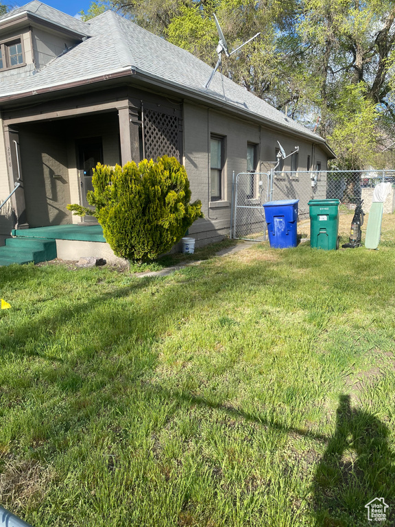 View of property exterior with fence, a lawn, brick siding, and roof with shingles