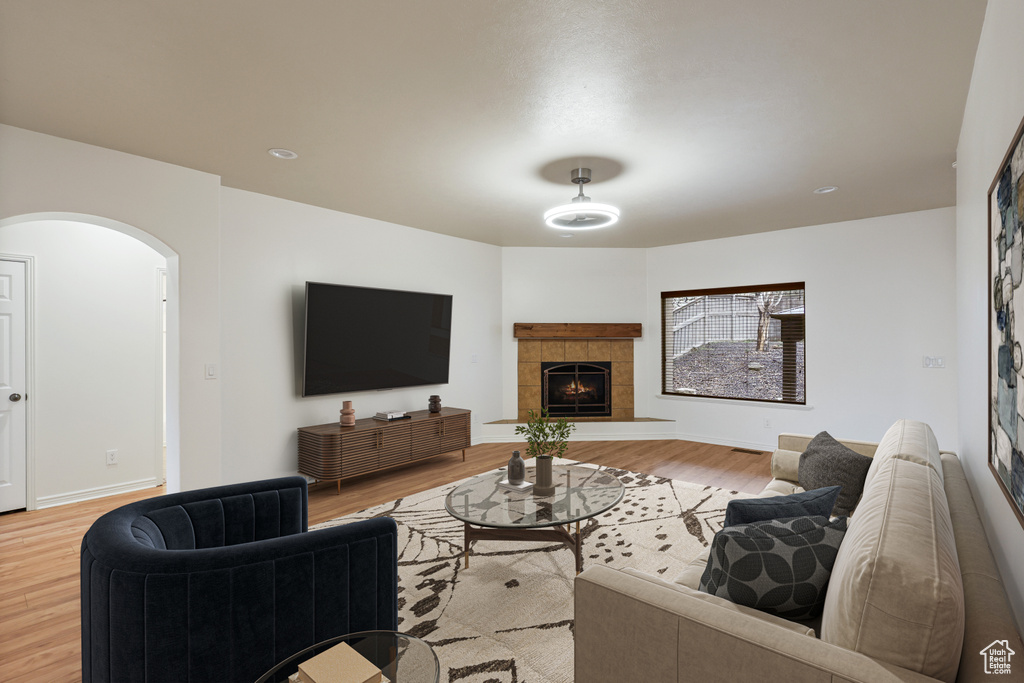 Living area with light wood-type flooring, arched walkways, a tiled fireplace, and baseboards