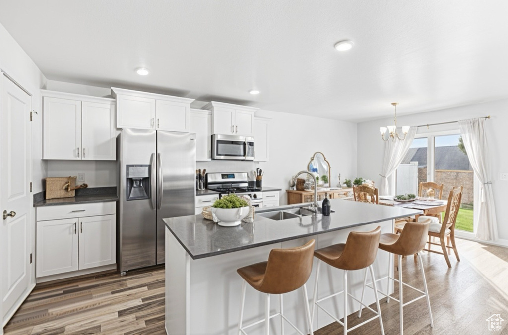 Kitchen with appliances with stainless steel finishes, a sink, light wood-style floors, a chandelier, and dark countertops