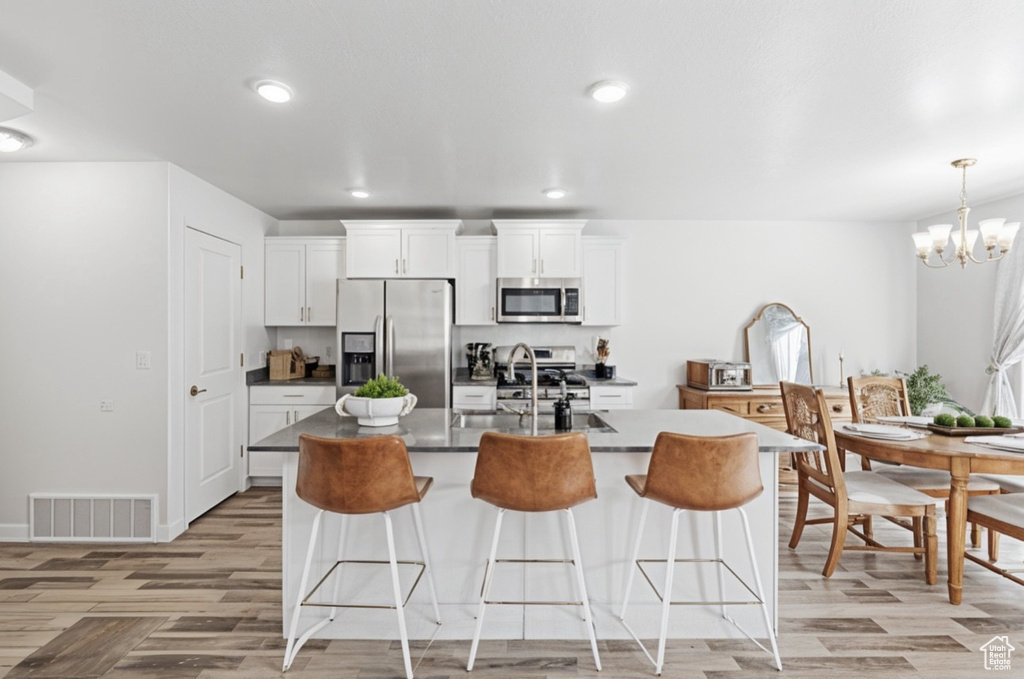 Kitchen featuring appliances with stainless steel finishes, a sink, a kitchen bar, dark countertops, and light wood-style flooring