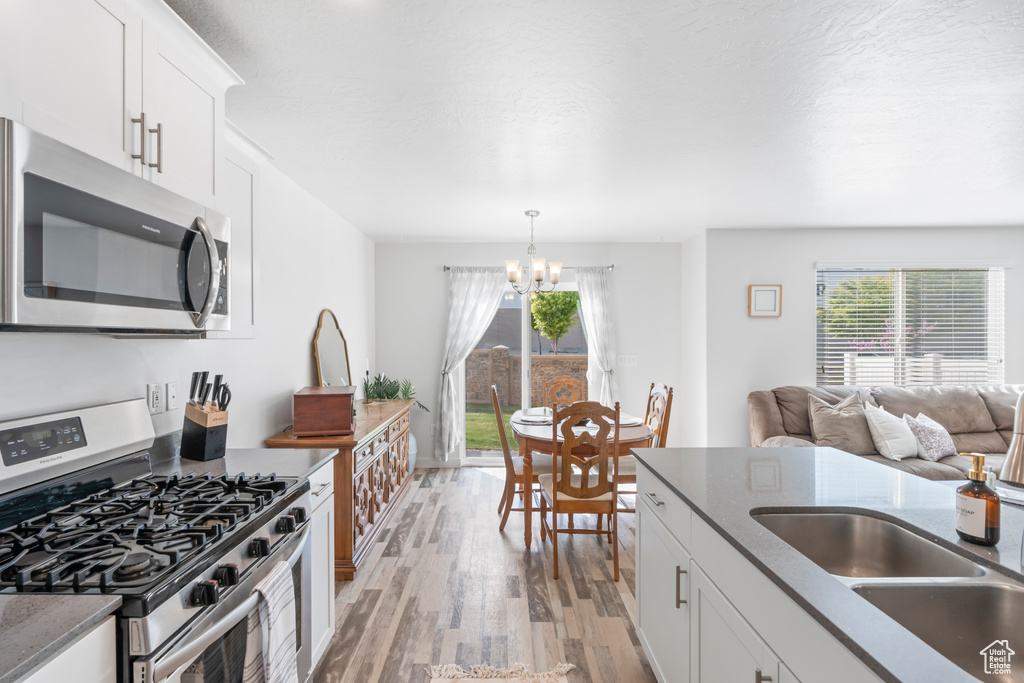 Kitchen with a sink, a chandelier, a wealth of natural light, stainless steel appliances, and light wood finished floors