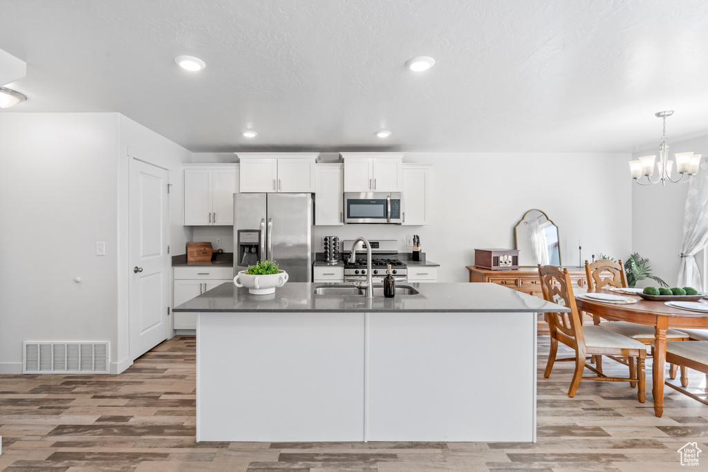 Kitchen with stainless steel appliances, light wood-style flooring, a sink, dark countertops, and visible vents