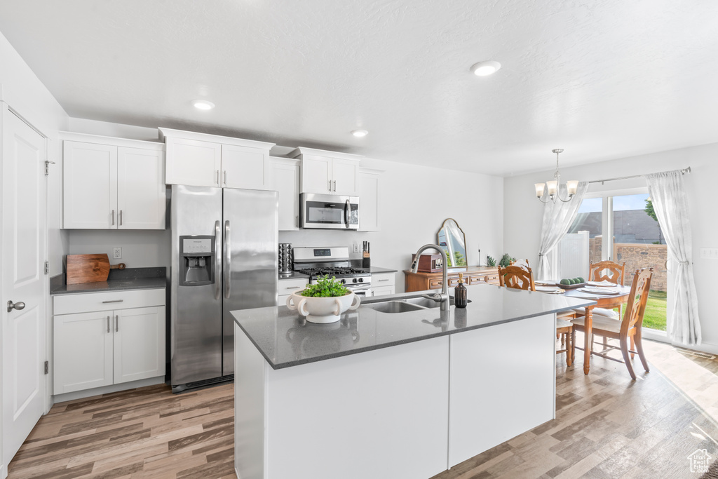 Kitchen with appliances with stainless steel finishes, a chandelier, light wood-type flooring, and a sink