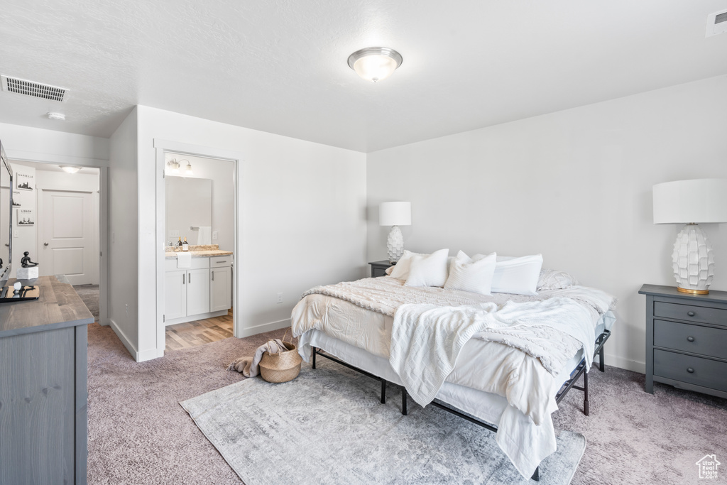Bedroom with visible vents, baseboards, light carpet, and ensuite bathroom
