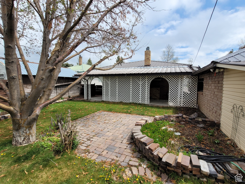 Back of property featuring a chimney, a patio area, metal roof, and brick siding