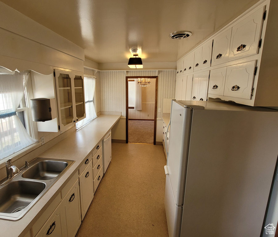 Kitchen with white appliances, a sink, white cabinets, a chandelier, and light countertops