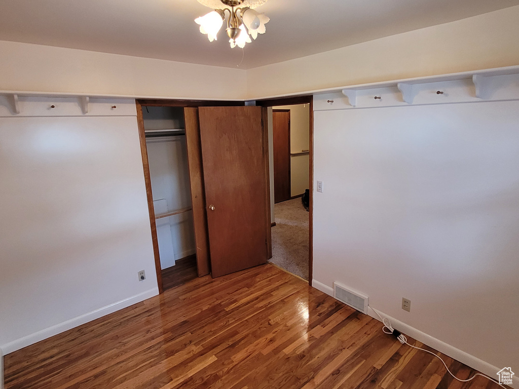 Unfurnished bedroom featuring wood finished floors, baseboards, a closet, and a chandelier