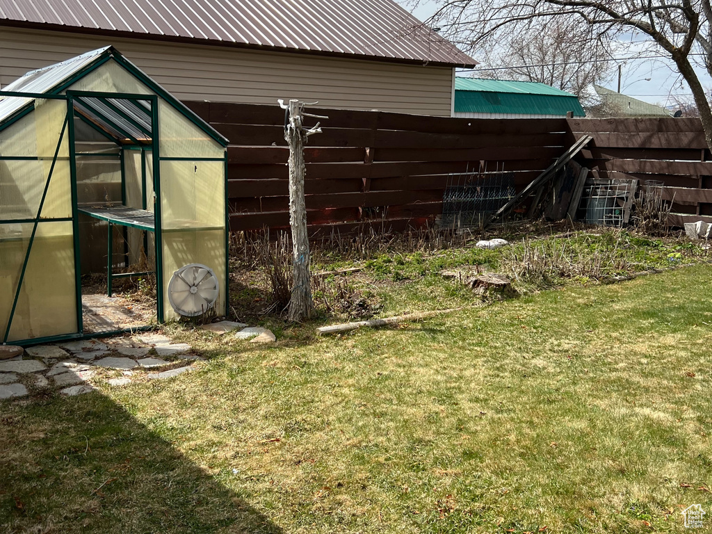 View of grassy yard featuring a greenhouse and an outbuilding