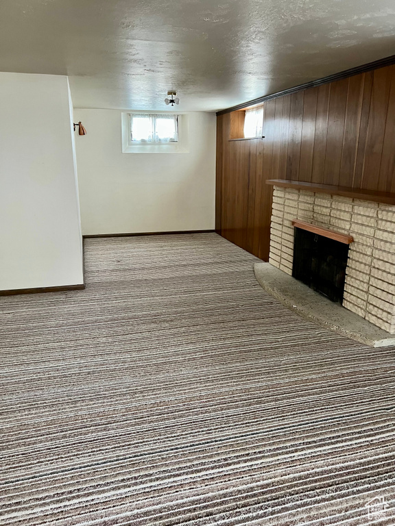 Basement with wood walls, a brick fireplace, a textured ceiling, and carpet