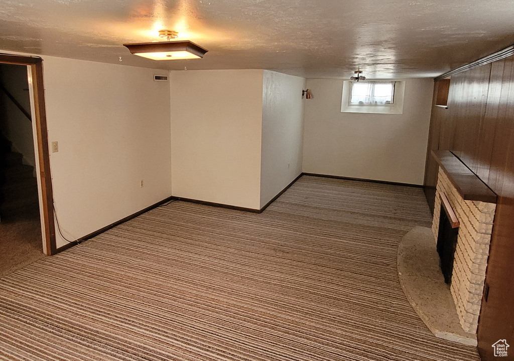 Basement with carpet flooring, a fireplace with raised hearth, stairway, baseboards, and a textured ceiling