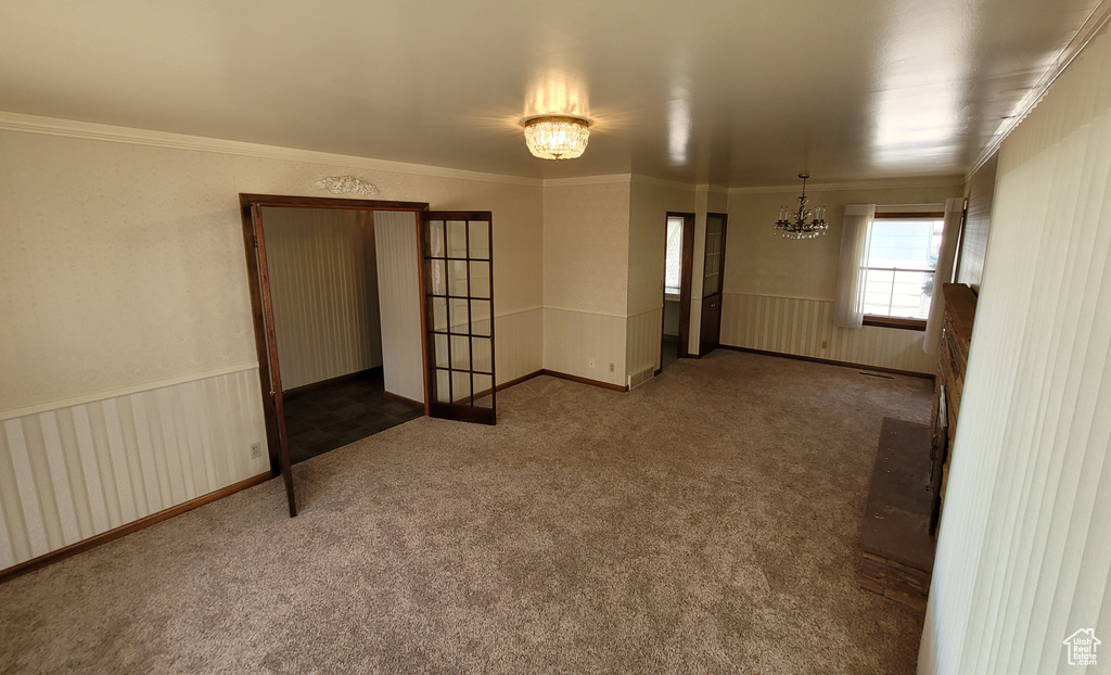Carpeted empty room with a chandelier, crown molding, radiator, and wainscoting