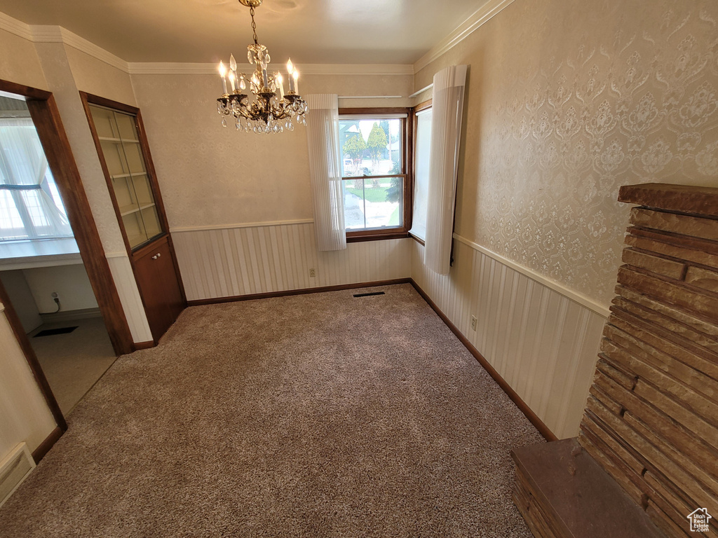 Carpeted spare room with a chandelier, ornamental molding, and wainscoting