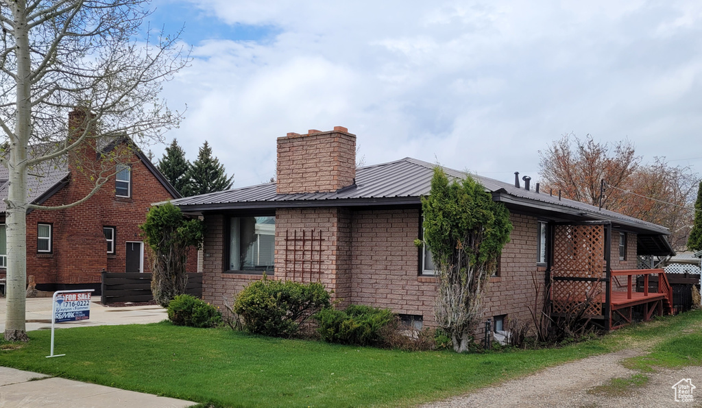 View of front of property with a chimney, a front yard, metal roof, and brick siding