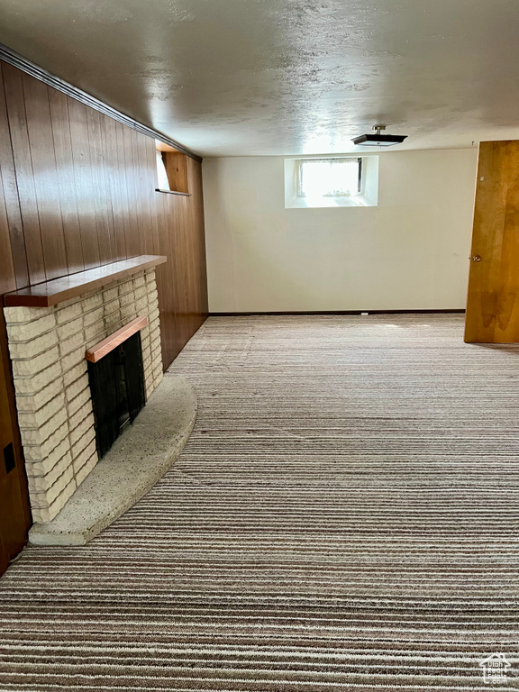 Basement featuring carpet floors, a textured ceiling, wooden walls, and a fireplace