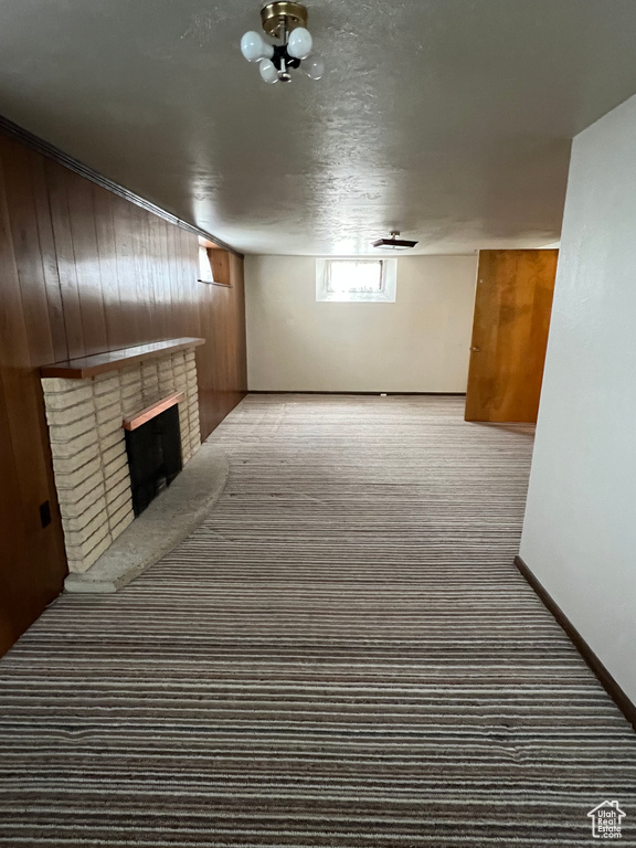 Below grade area featuring carpet flooring, a fireplace, wood walls, and baseboards