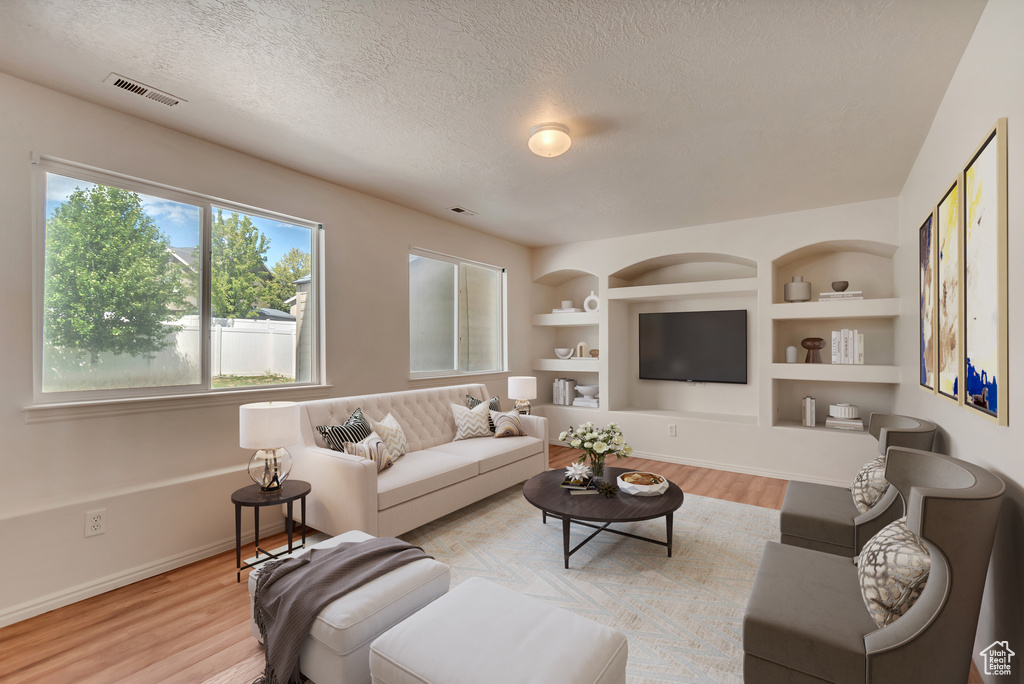 Living room featuring light wood-style floors, a textured ceiling, baseboards, and built in features