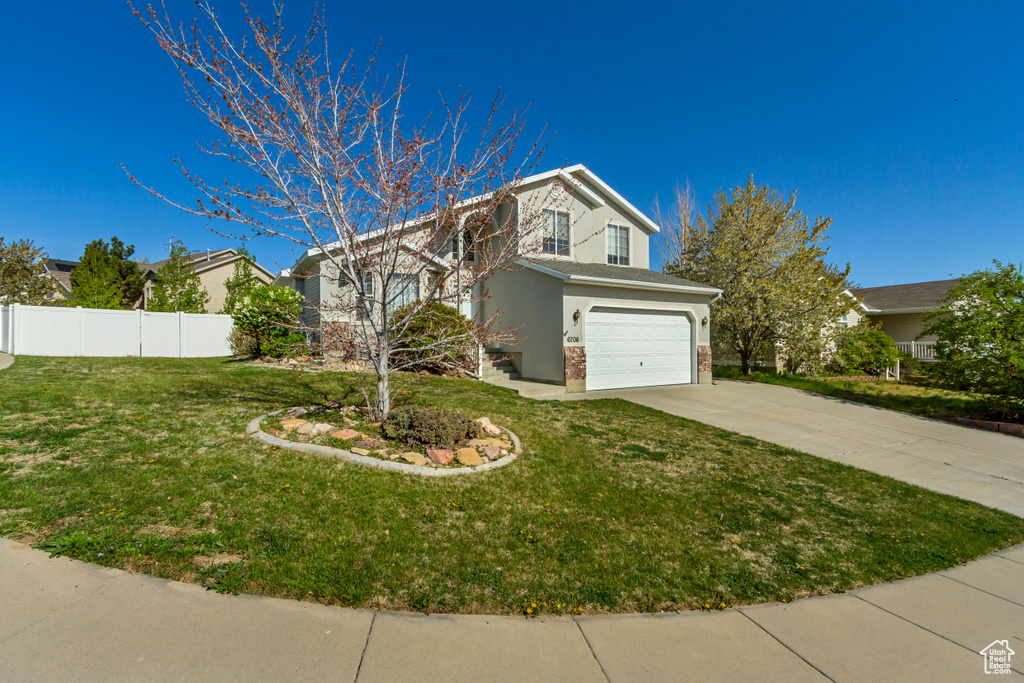 Traditional home featuring fence, a front lawn, stucco siding, an attached garage, and driveway