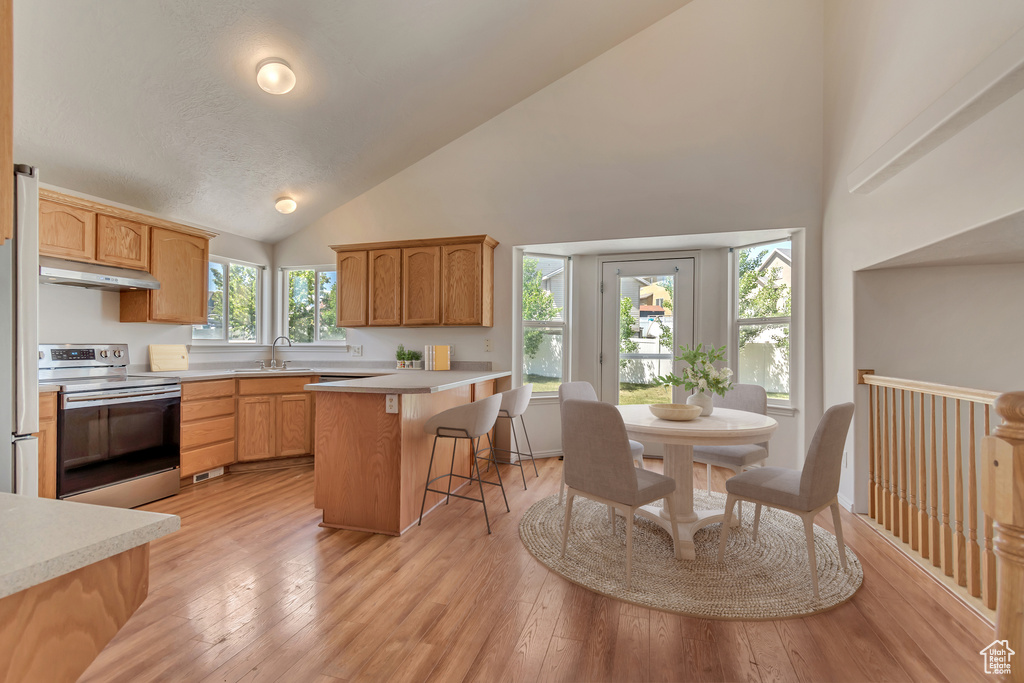 Kitchen with stainless steel range with electric stovetop, under cabinet range hood, high vaulted ceiling, a sink, and a kitchen bar