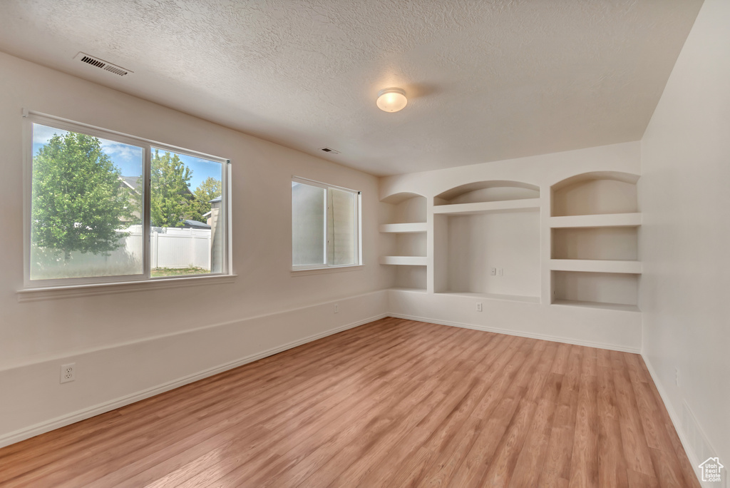 Spare room featuring a textured ceiling, baseboards, and light wood-type flooring