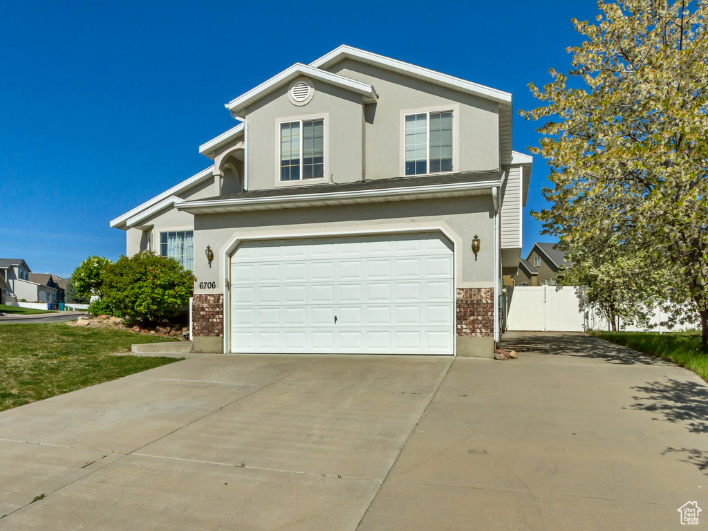 Traditional home with stucco siding, concrete driveway, brick siding, a front yard, and a garage