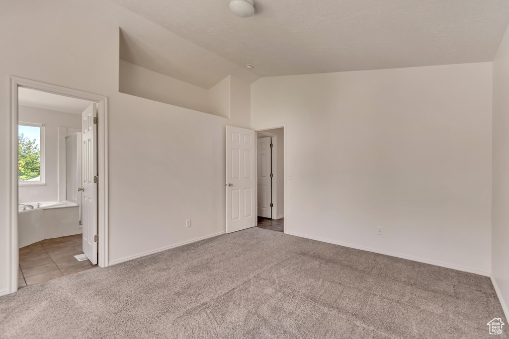 Unfurnished bedroom featuring carpet, ensuite bathroom, baseboards, and lofted ceiling