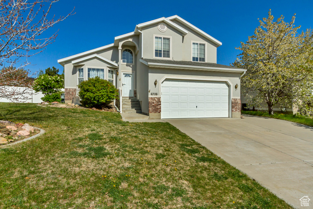 Traditional home with a front lawn, stucco siding, concrete driveway, brick siding, and a garage