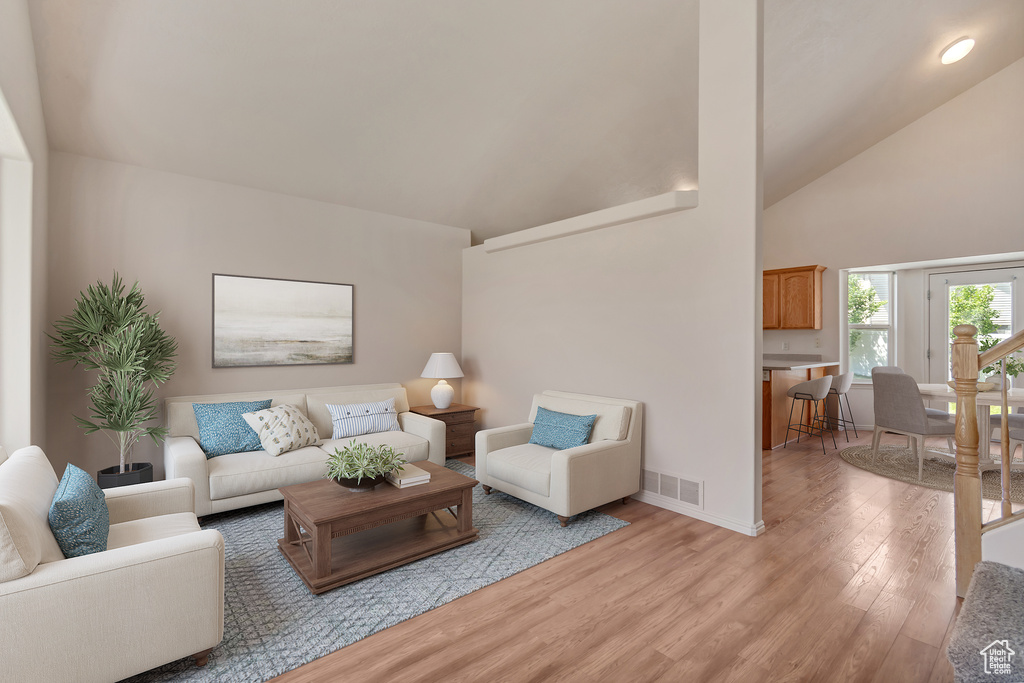 Living room with light wood finished floors, high vaulted ceiling, and baseboards