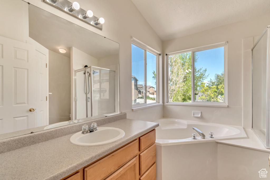 Full bathroom with a stall shower, vanity, lofted ceiling, and a bath