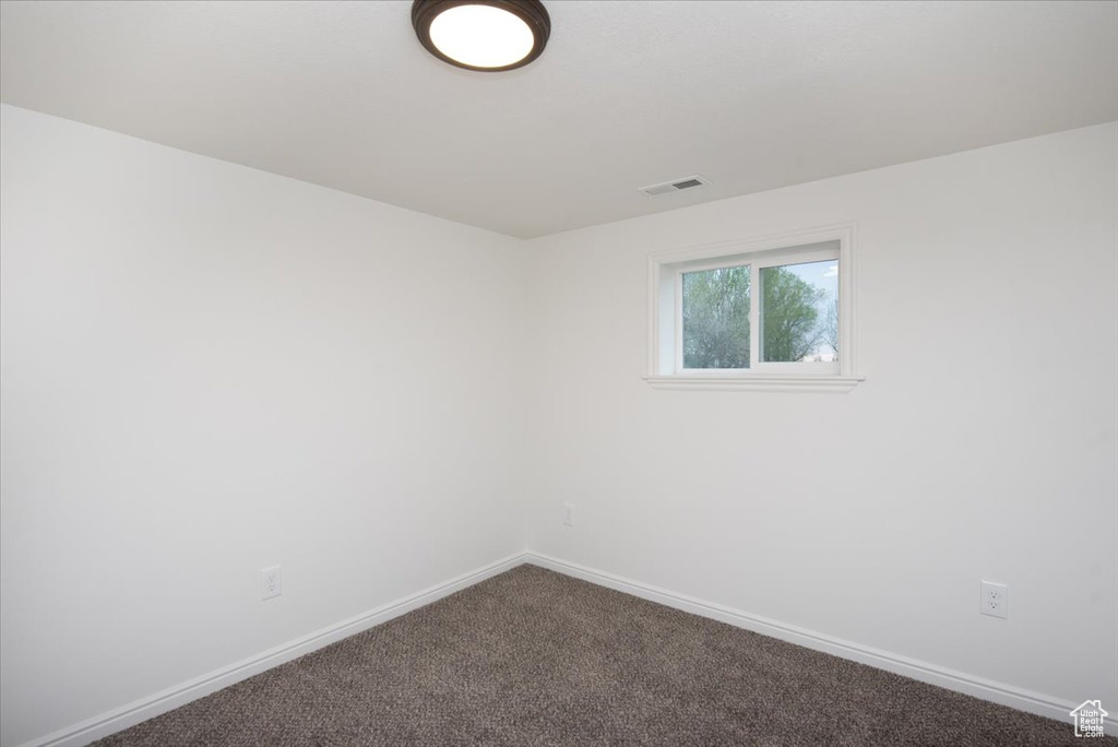 Empty room featuring baseboards, dark colored carpet, and visible vents