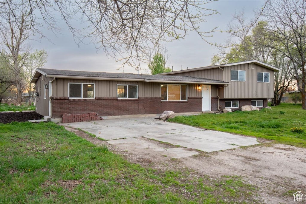 Split level home with board and batten siding, concrete driveway, a front yard, and brick siding
