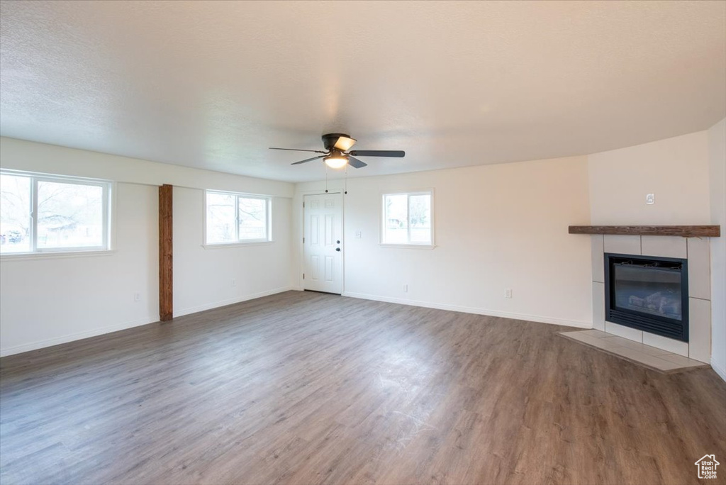 Unfurnished living room with baseboards, ceiling fan, a tiled fireplace, and wood finished floors