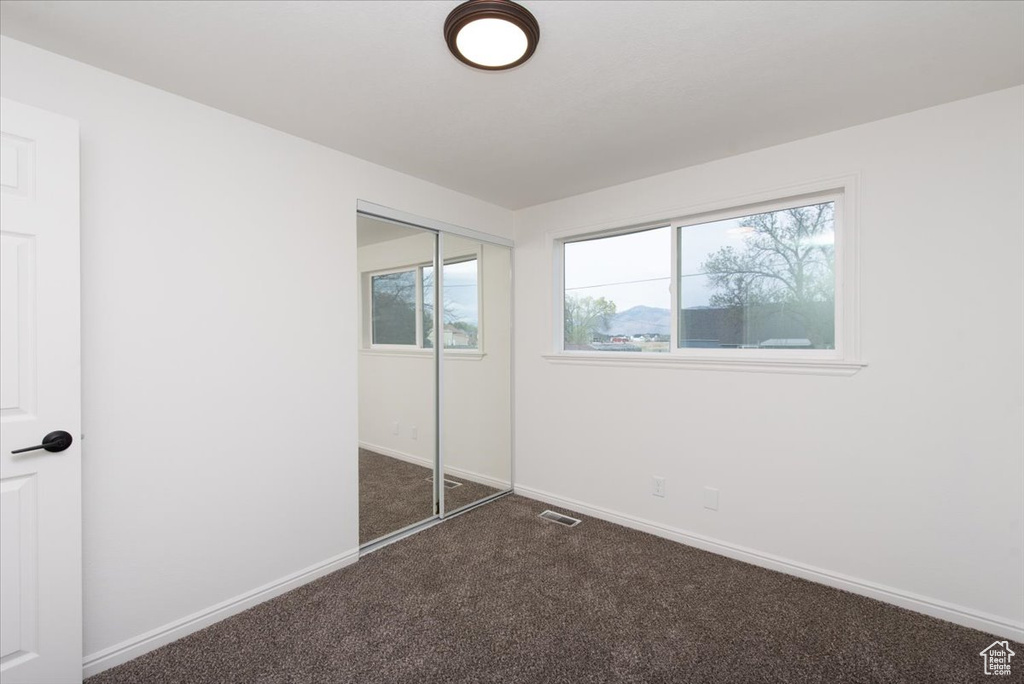 Unfurnished bedroom featuring baseboards, a closet, dark carpet, and visible vents