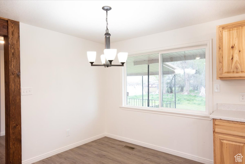 Unfurnished dining area featuring baseboards, wood finished floors, and a notable chandelier