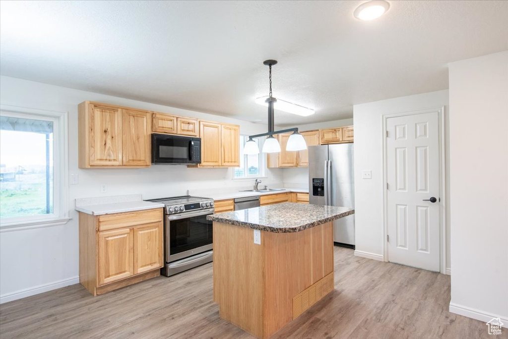 Kitchen with a kitchen island, light brown cabinets, light wood-style floors, a sink, and stainless steel appliances