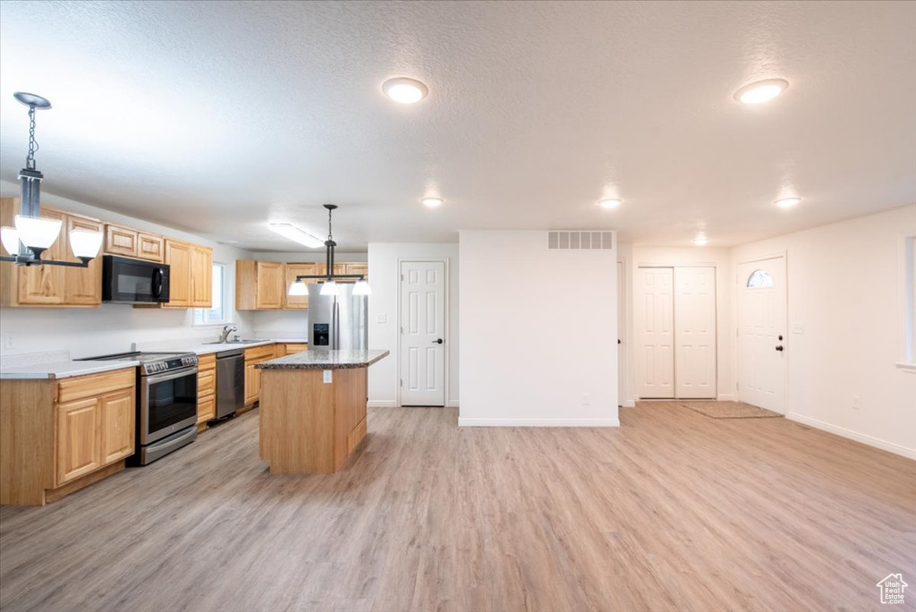 Kitchen with appliances with stainless steel finishes, a sink, light wood-style flooring, baseboards, and a kitchen island
