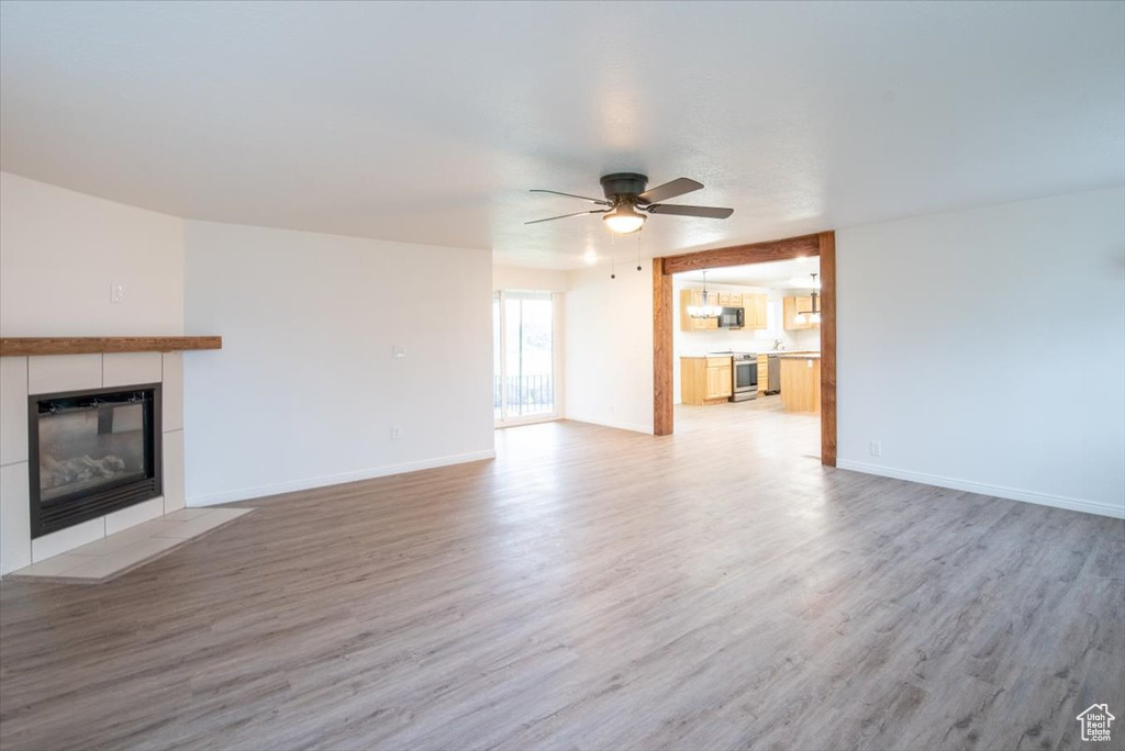Unfurnished living room featuring a tiled fireplace, baseboards, a ceiling fan, and light wood-style flooring