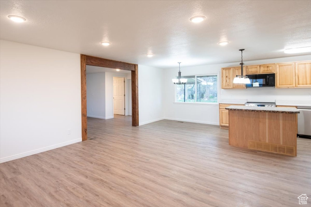 Kitchen featuring black microwave, light brown cabinets, a center island, baseboards, and light wood-type flooring
