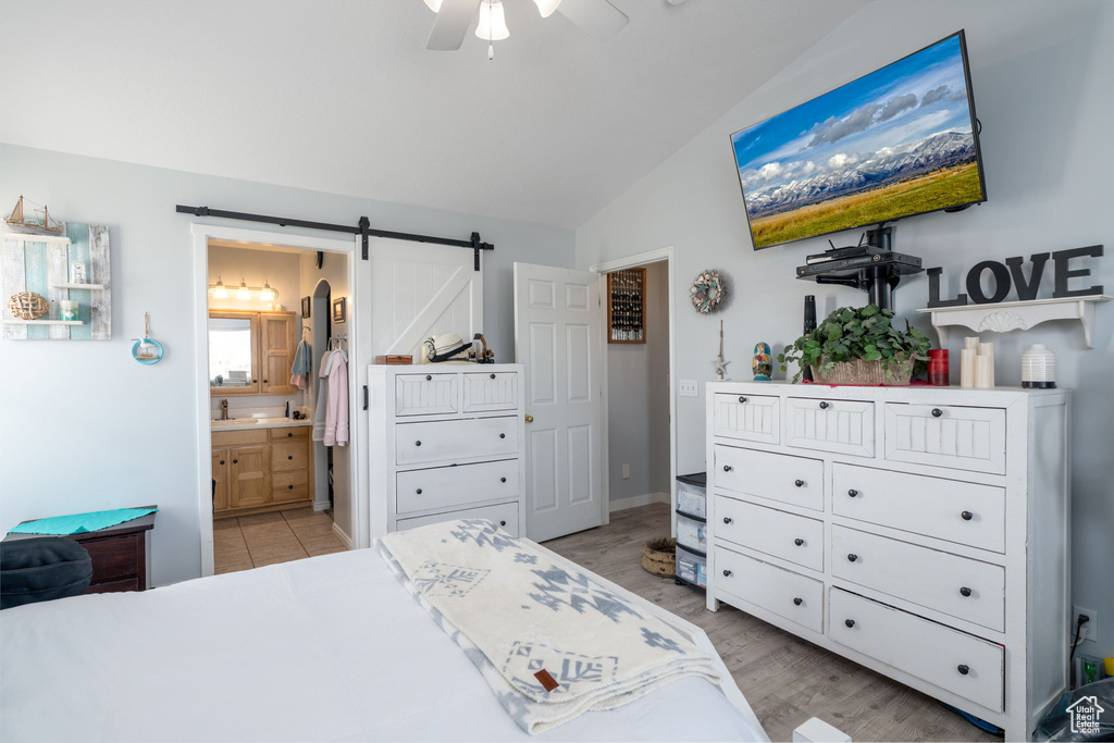 Bedroom with light wood-style flooring, a barn door, ensuite bathroom, lofted ceiling, and a ceiling fan