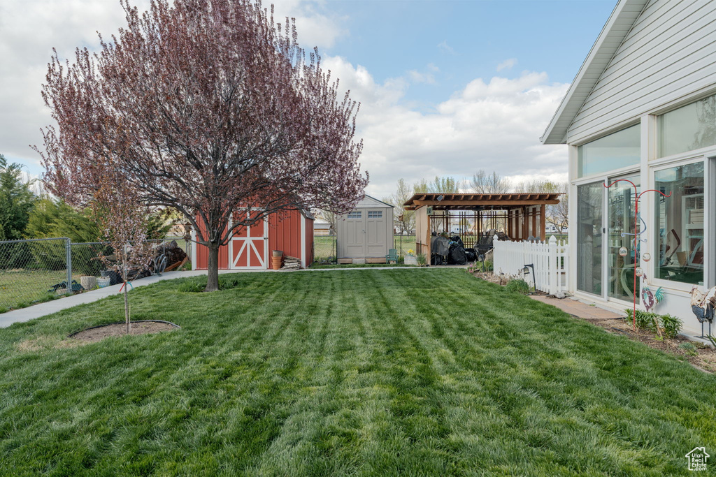 View of yard featuring a storage shed, an outbuilding, a pergola, and fence