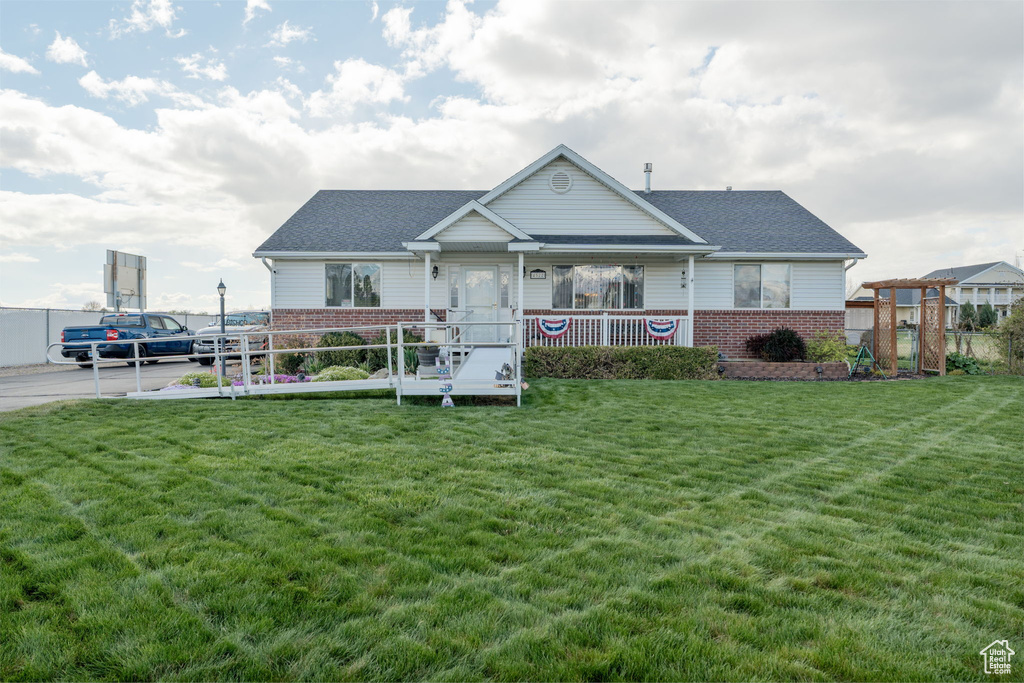 View of front of home with brick siding, a shingled roof, a front yard, and fence