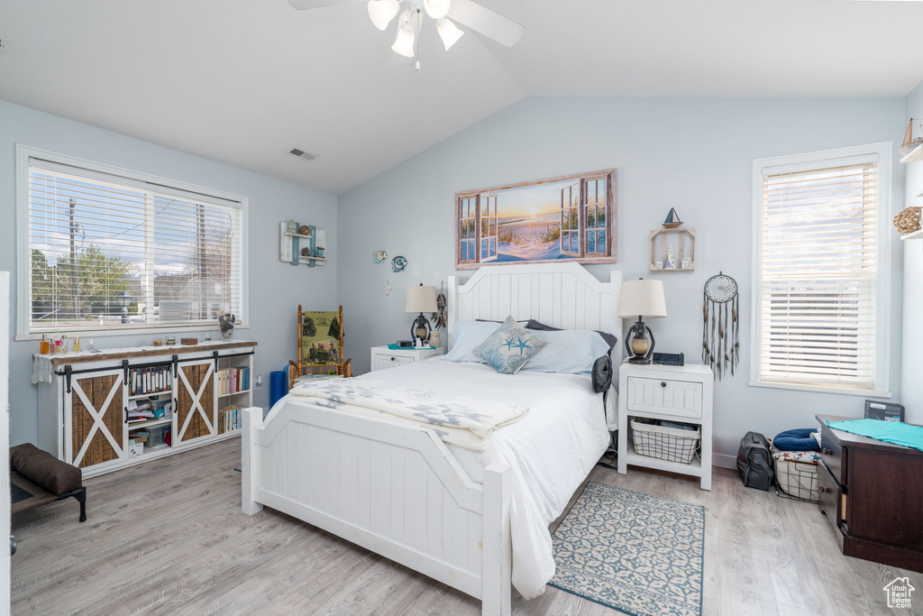 Bedroom featuring multiple windows, lofted ceiling, visible vents, and wood finished floors