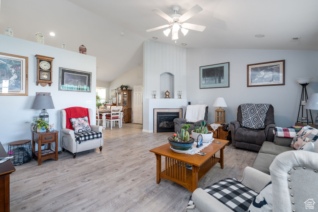 Living area with light wood-type flooring, a ceiling fan, a fireplace, and high vaulted ceiling